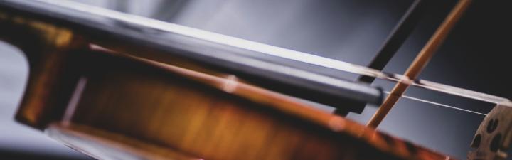 Close up of a violin being played against a black and gray abstract background.